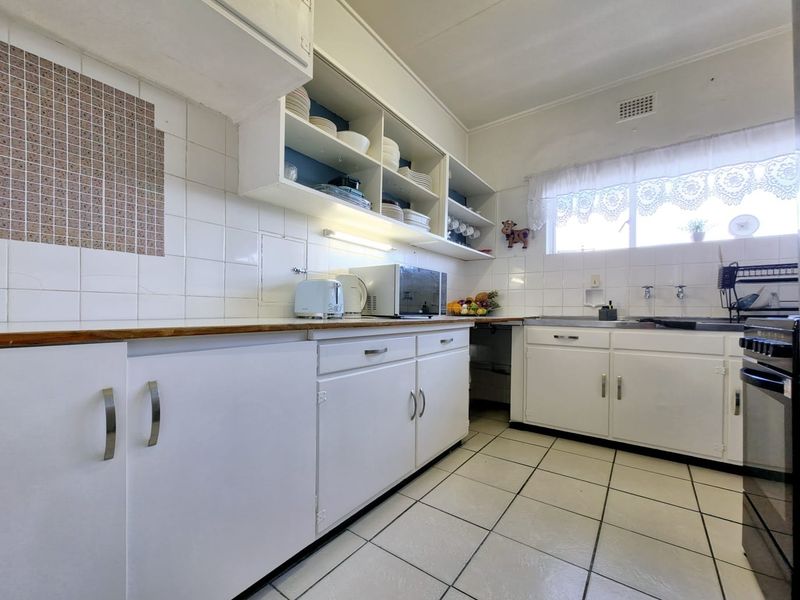 A dated kitchen featuring white cabinetry, tiled backsplash, and tiled flooring, offering a functional layout with potential for modern renovation.