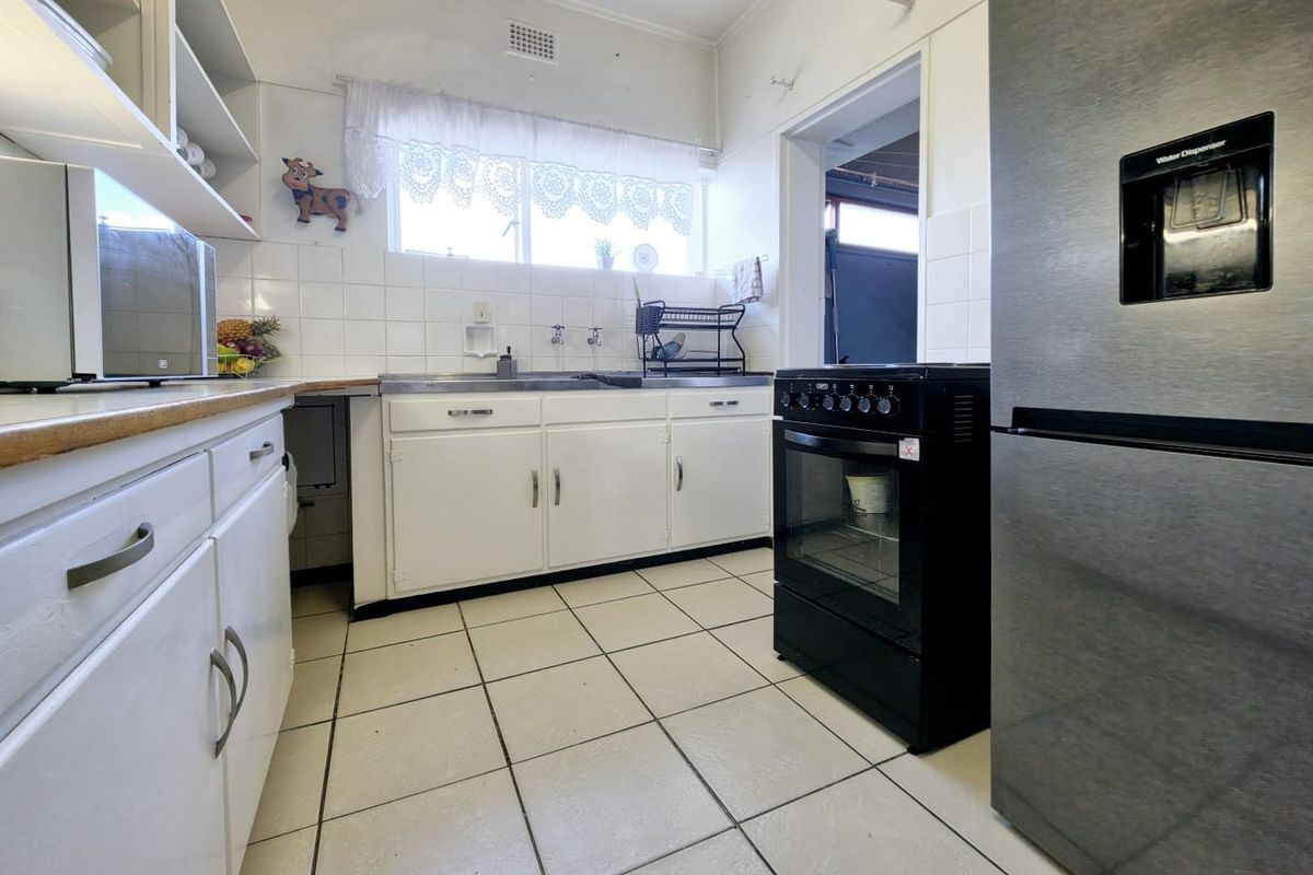 A functional kitchen featuring white cabinetry, tiled backsplash, tiled flooring, and a freestanding oven, offering a practical layout with potential for modern updates.