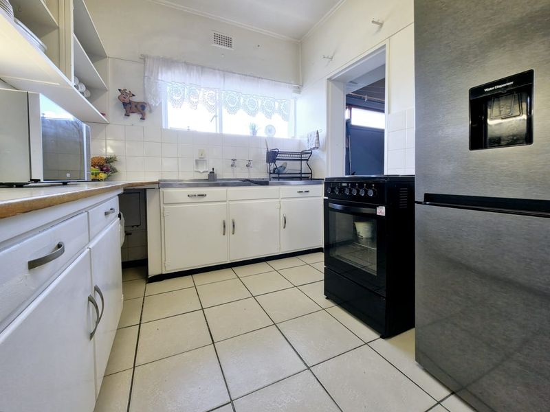 A functional kitchen featuring white cabinetry, tiled backsplash, tiled flooring, and a freestanding oven, offering a practical layout with potential for modern updates.