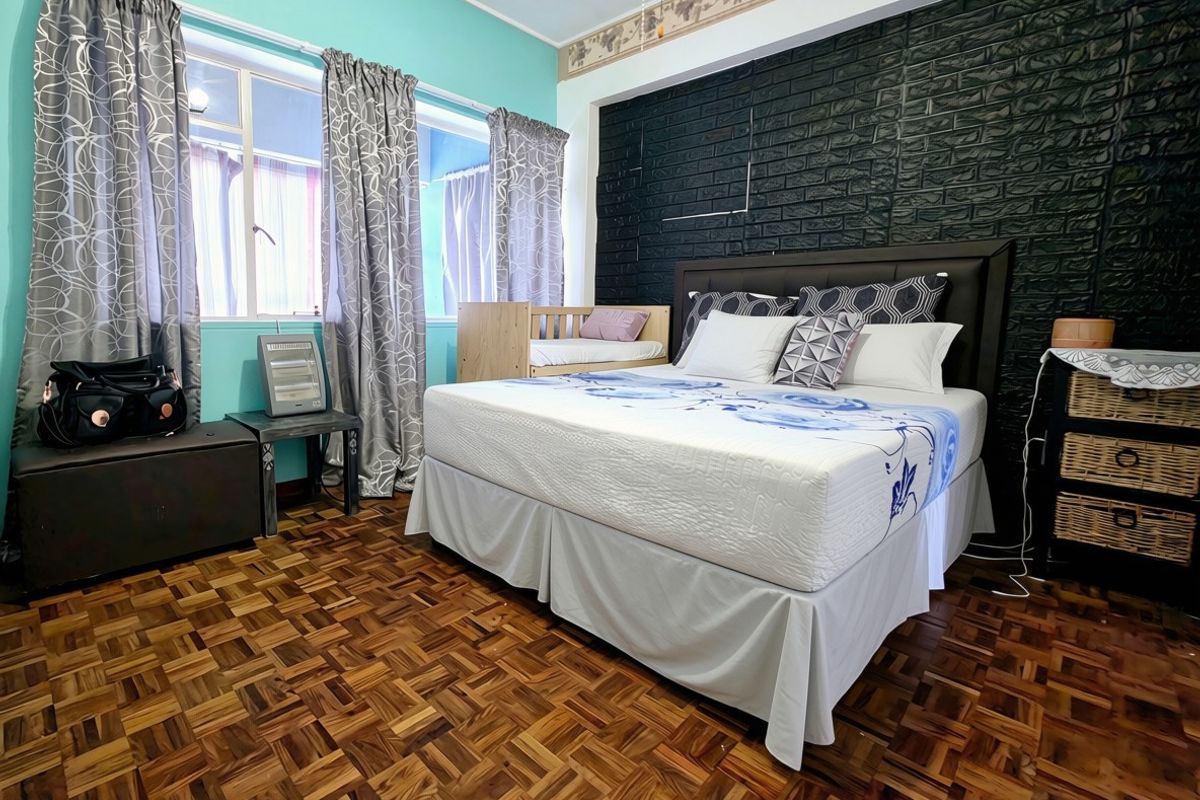 Spacious bedroom featuring classic parquet flooring, a bold black brick feature wall, and large windows allowing for natural light.