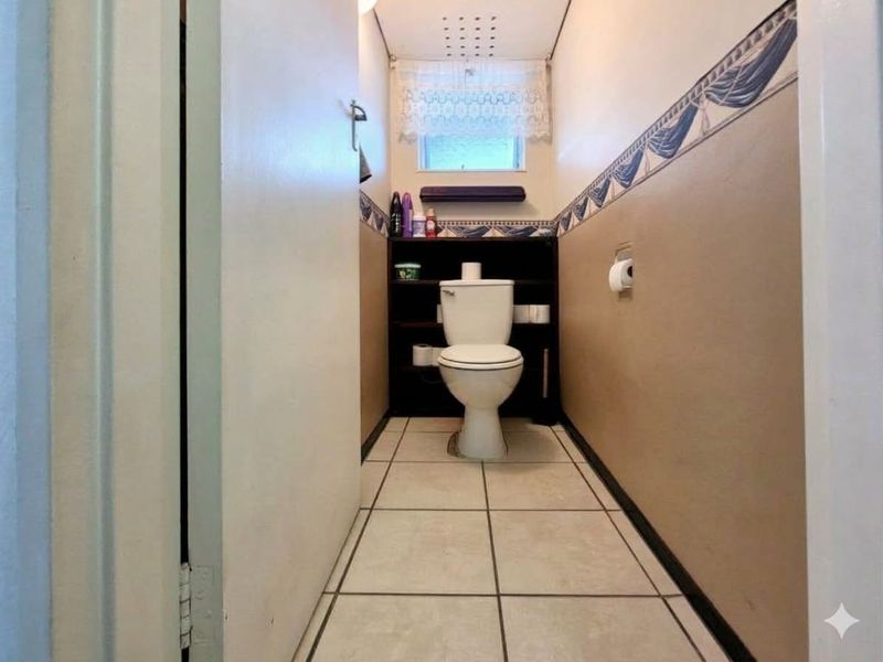 A compact bathroom featuring tiled flooring, a standard toilet, and decorative wall trim, offering a functional space with potential for modern updates.
