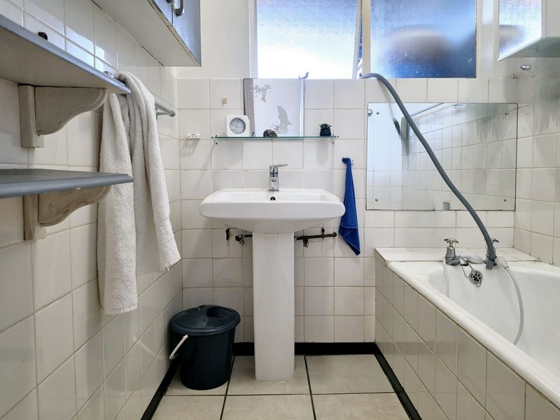 A dated bathroom featuring a pedestal basin, built-in bathtub, and tiled finishes, offering potential for modernization and renovation.