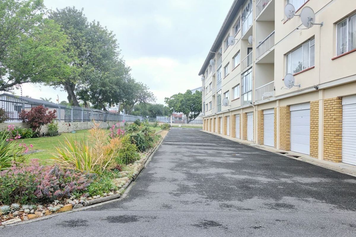 Exterior view of the apartment complex featuring a paved driveway, ground-level garage access, and a landscaped garden area along the building perimeter.