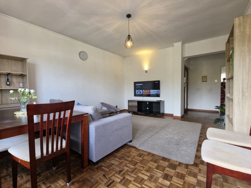 A well-lit living room featuring classic parquet flooring, neutral walls, and a functional layout suitable for comfortable daily living.