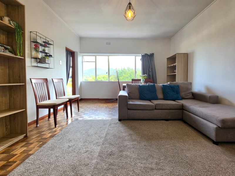 A bright living room featuring classic parquet flooring, large windows providing natural light, and a neutral layout suitable for various interior design styles.