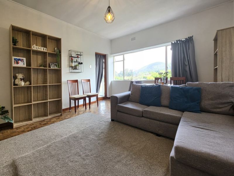 A bright living room featuring classic parquet flooring, a large window with natural light, and a neutral color palette.