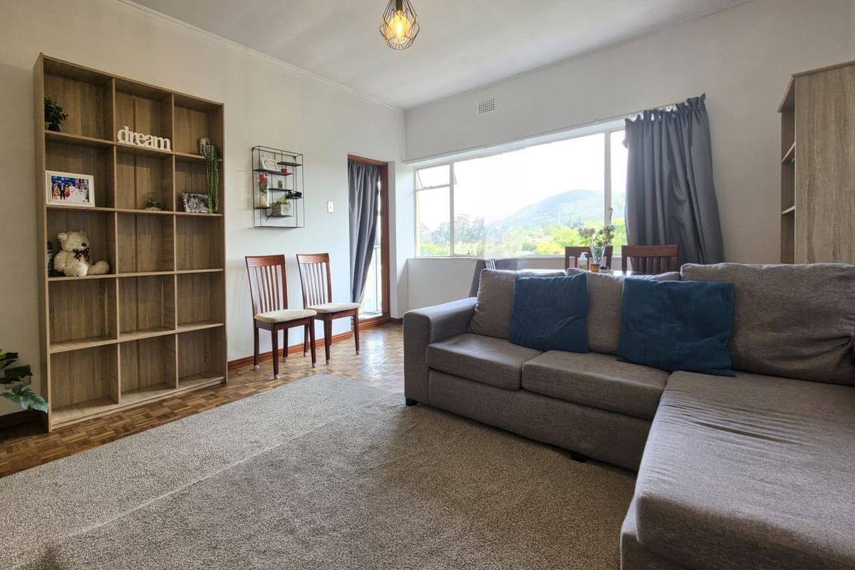 A bright living room featuring classic parquet flooring, a large window with natural light, and a neutral color palette.