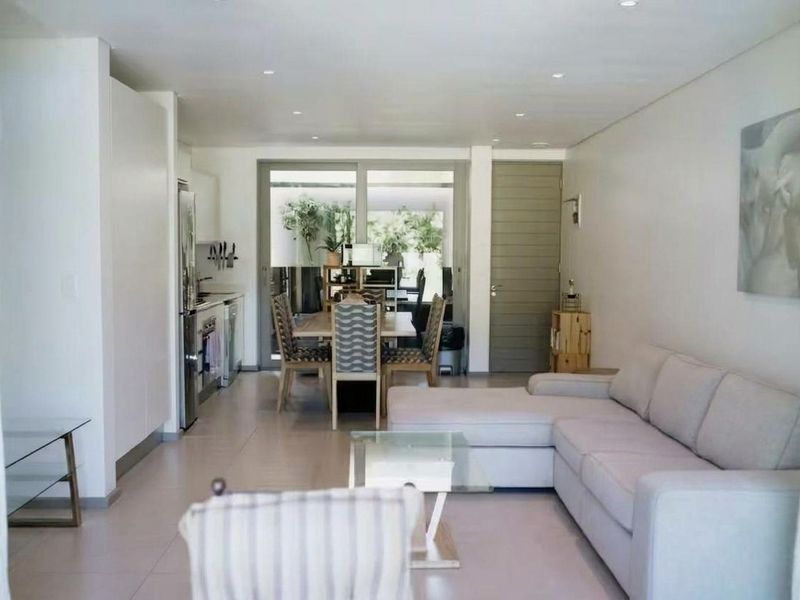 A bright open-plan living and dining area featuring tiled floors, recessed lighting, and seamless access to an outdoor patio through sliding glass doors.