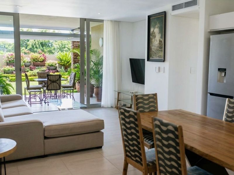 Modern open-plan living and dining area featuring tiled floors, recessed lighting, and large sliding glass doors opening onto a landscaped patio.
