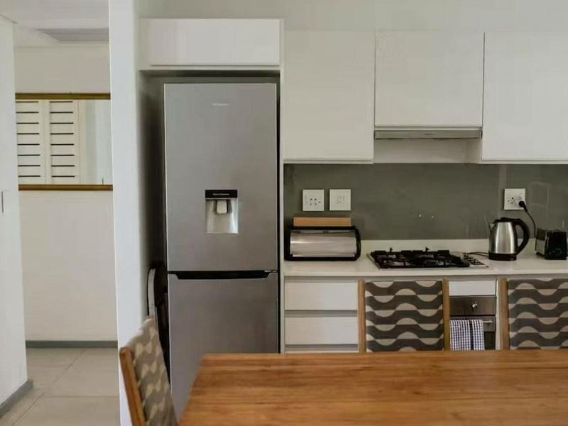 Modern kitchen featuring white cabinetry, stone countertops, glass splashback, and integrated gas hob with extractor fan.
