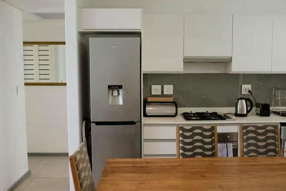 Modern kitchen featuring white cabinetry, stone countertops, glass splashback, and integrated gas hob with extractor fan.