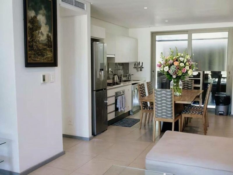 Modern open-plan kitchen and dining area featuring sleek cabinetry, integrated appliances, tiled flooring, and large sliding doors leading to an outdoor space.
