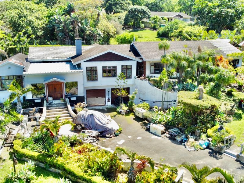 Aerial view of a residential property featuring a multi-level house, double garage, paved driveway, and extensive landscaped gardens.