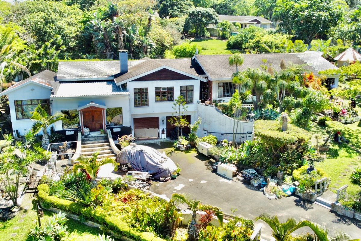 Aerial view of a residential property featuring a multi-level house, double garage, paved driveway, and extensive landscaped gardens.