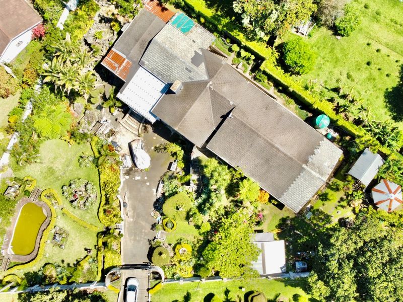 Aerial view of a residential property featuring a large landscaped garden, driveway, pond, and a main house with a tiled roof.