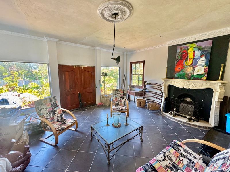 Spacious living room featuring a classic fireplace with an ornate mantel, decorative ceiling rose, and dark tiled flooring with large windows.