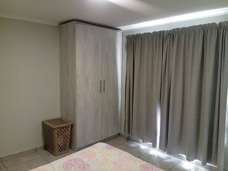 A bedroom featuring neutral-toned tiled flooring and a built-in wardrobe with a light wood-grain finish.