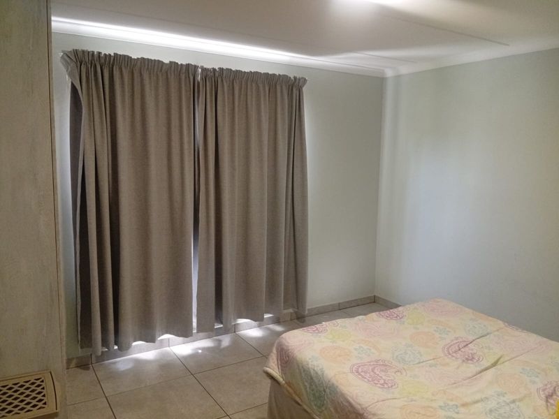 A simple bedroom featuring tiled flooring and a built-in cupboard, providing a functional and neutral space.