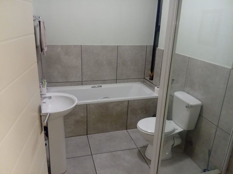 A functional bathroom featuring a pedestal basin, a built-in bathtub with tiled surround, and a standard toilet, finished with neutral floor and wall tiles.