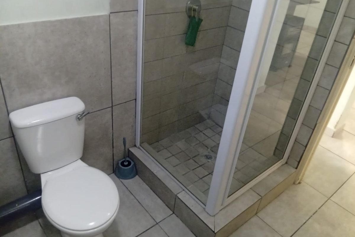 A functional bathroom featuring a white toilet and a glass-enclosed shower with neutral wall and floor tiling.