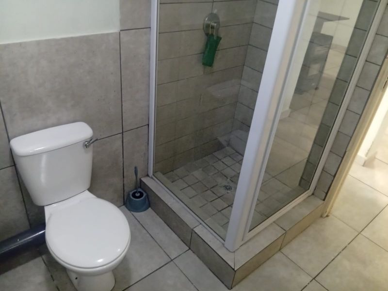 A functional bathroom featuring a white toilet and a glass-enclosed shower with neutral wall and floor tiling.