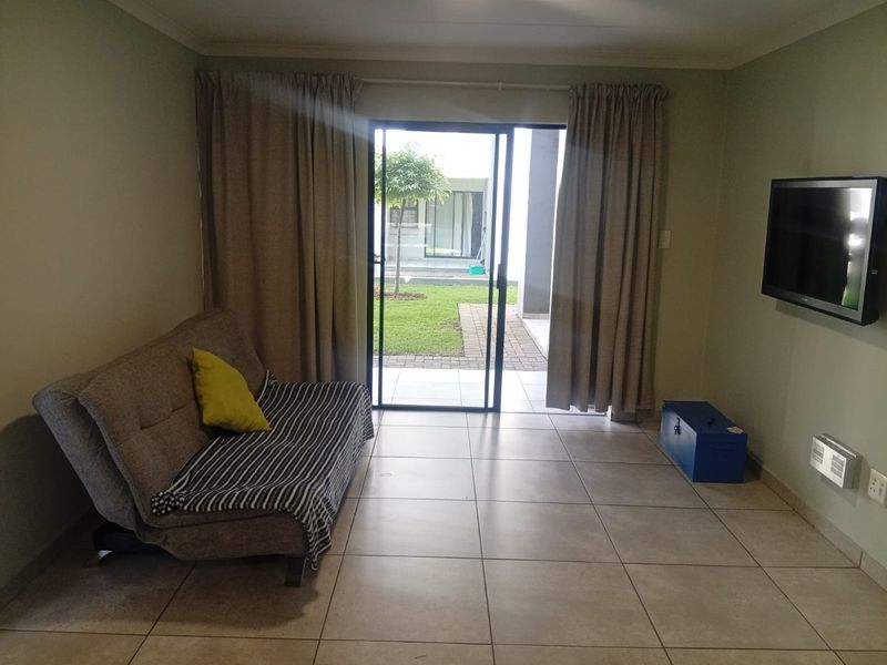 A living room featuring tiled flooring and a sliding glass door providing direct access to the outdoor garden area.