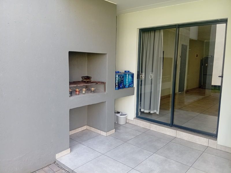 A covered patio area featuring a built-in braai and large sliding glass doors providing access to the interior living space.