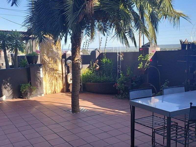 A private outdoor patio area featuring tiled flooring, enclosed by a boundary wall with integrated electric fencing and established garden elements.