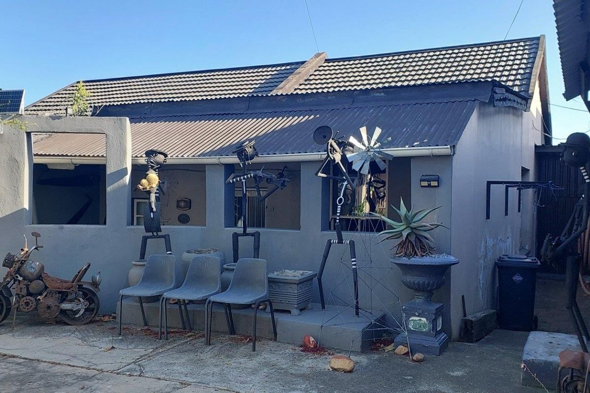 Rear exterior view of the property featuring a covered patio area with concrete flooring and a combination of tiled and corrugated metal roofing.