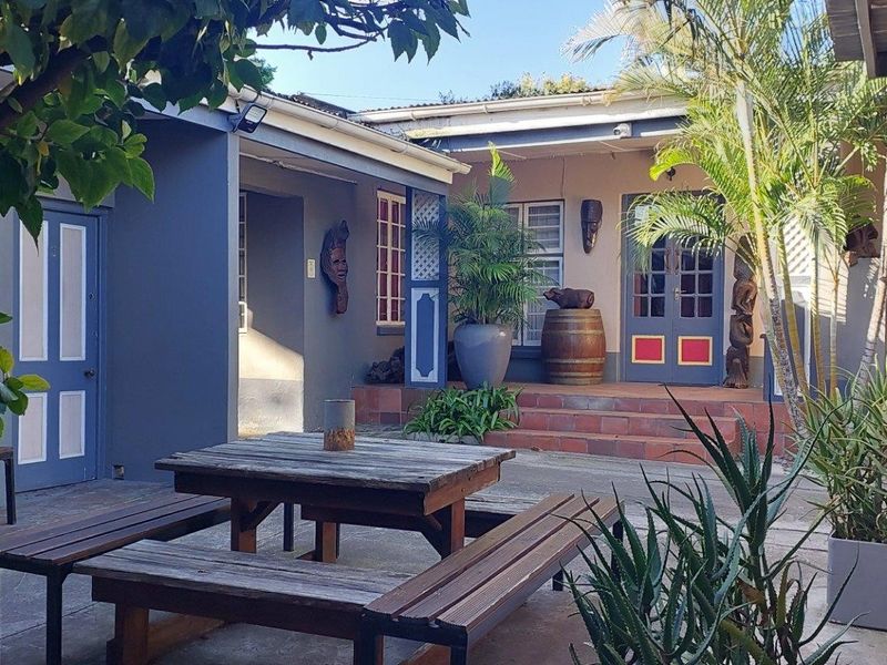 A paved outdoor patio area featuring tiled steps leading to double and single entrance doors, surrounded by established garden greenery.