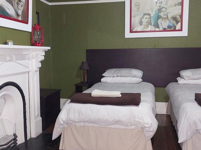 A bedroom featuring a classic fireplace with a white mantelpiece and dark timber flooring, finished with green wall paint.