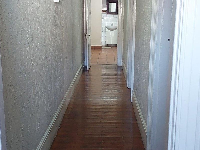 A long hallway featuring original timber flooring, a decorative archway, and high ceilings, leading towards a bathroom area.