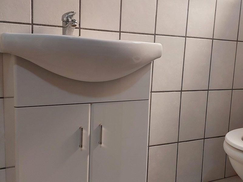 A functional bathroom featuring a white vanity cabinet with a basin and a standard toilet, finished with tiled walls.