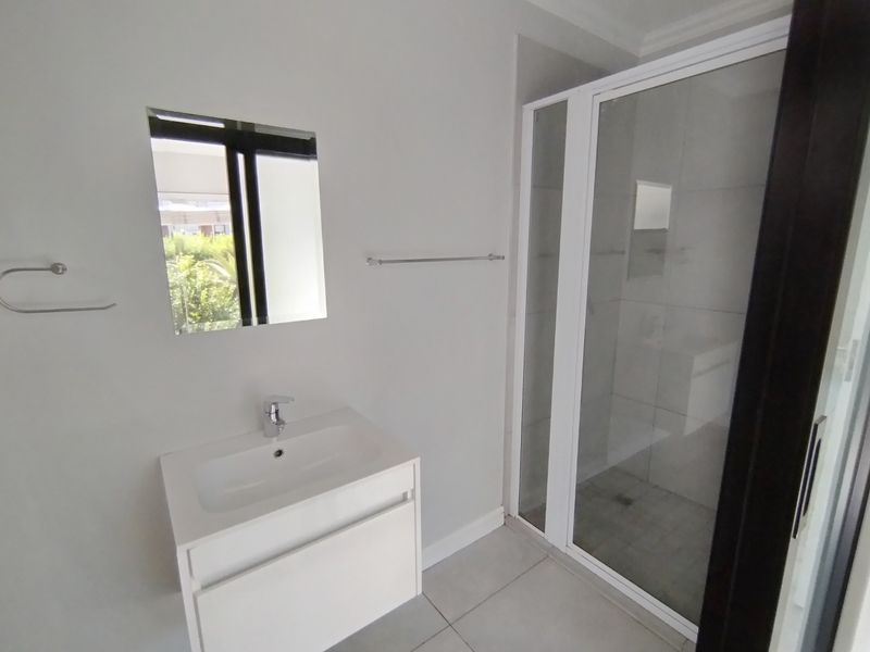 A clean, modern bathroom featuring a white vanity with basin, a glass-enclosed shower, and neutral floor tiling.