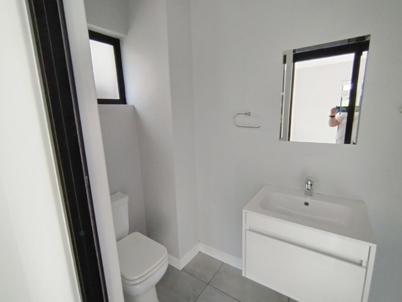 A clean, modern bathroom featuring a white vanity with basin, wall-mounted mirror, and a standard toilet with tiled flooring.