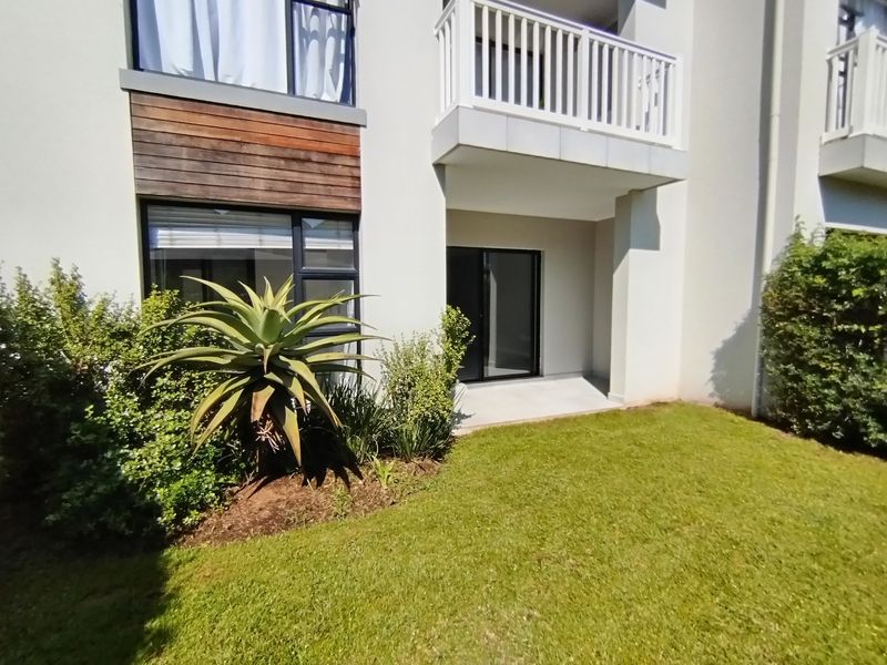 Rear view of the apartment building featuring a private balcony, sliding glass doors, and well-maintained garden area.