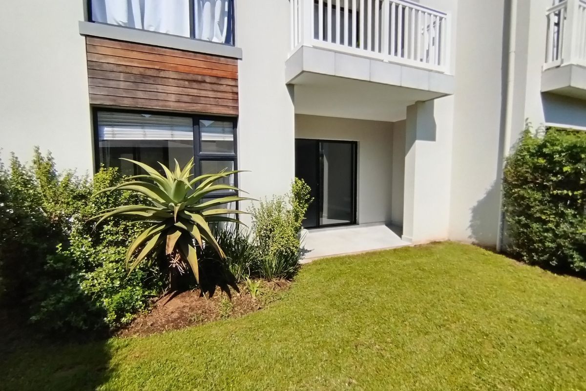 Rear view of the apartment building featuring a private balcony, sliding glass doors, and well-maintained garden area.