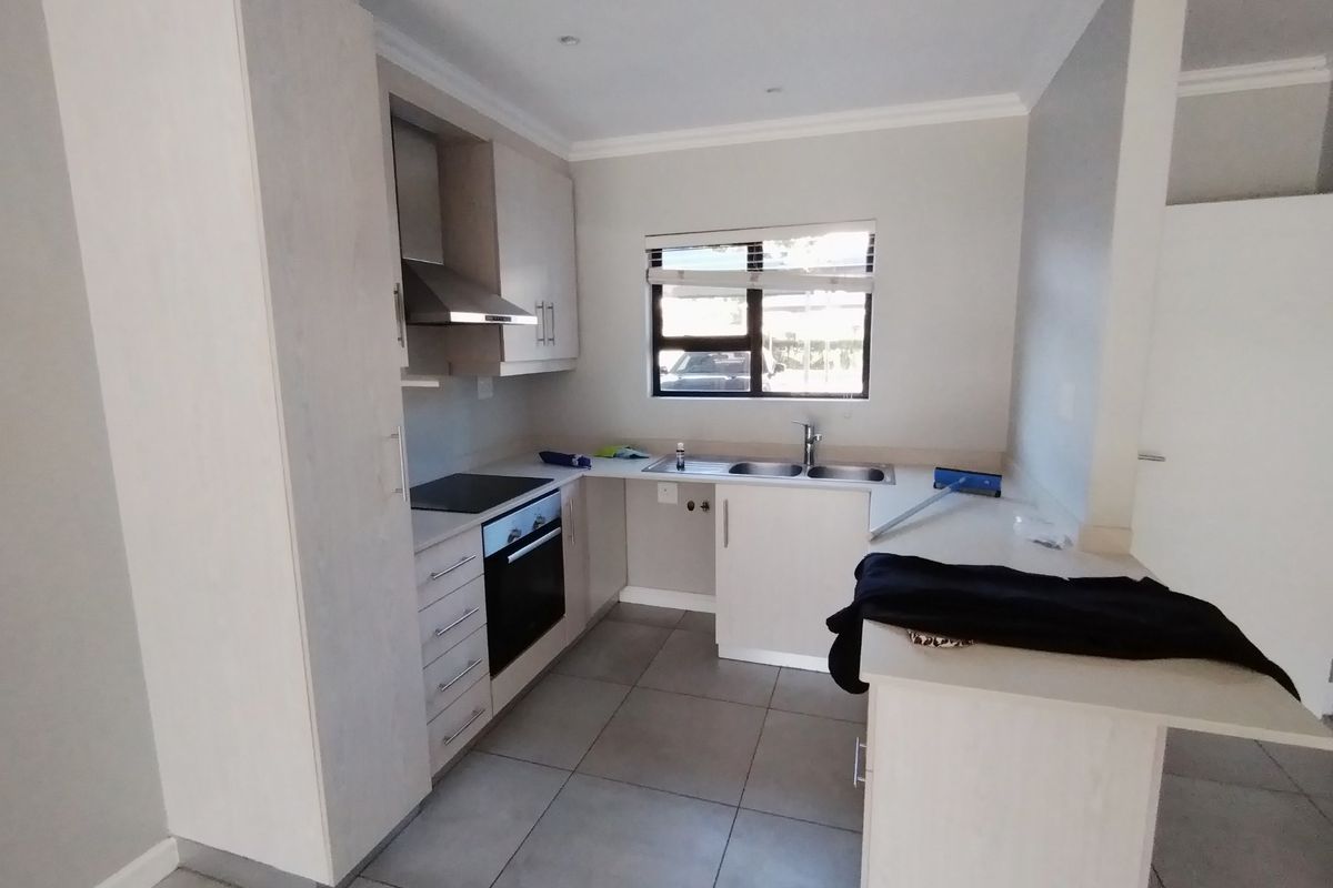 A clean, modern kitchen featuring light-toned cabinetry, built-in oven and hob, extractor fan, and tiled flooring, offering a functional and bright workspace.