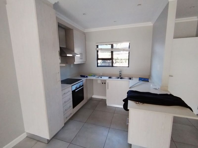 A clean, modern kitchen featuring light-toned cabinetry, built-in oven and hob, extractor fan, and tiled flooring, offering a functional and bright workspace.