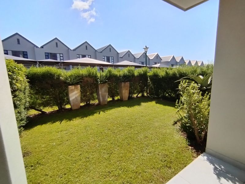 A well-maintained private garden featuring a manicured lawn and established hedge boundary, viewed from the adjacent patio area.