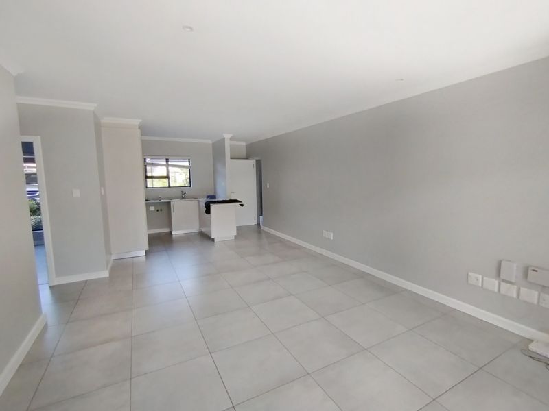Spacious open-plan living area featuring neutral tiled flooring, modern kitchen cabinetry, and recessed lighting, offering a clean and versatile blank canvas.