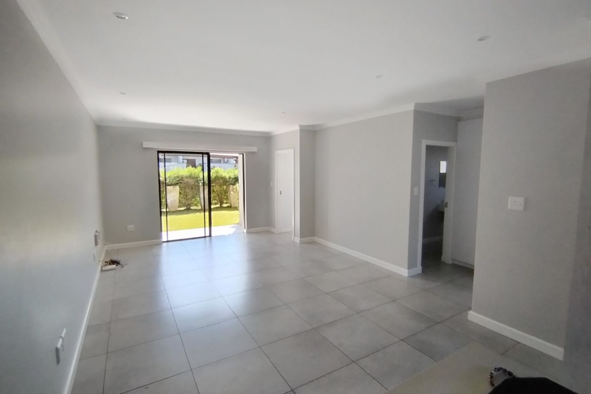A spacious, empty living area featuring neutral grey walls, large format floor tiles, and a sliding glass door providing access to the outdoor space.