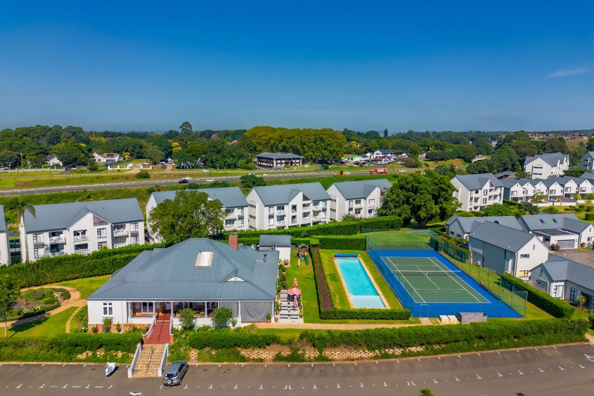 Aerial view of a residential apartment complex featuring a swimming pool, tennis court, landscaped gardens, and ample paved parking facilities.