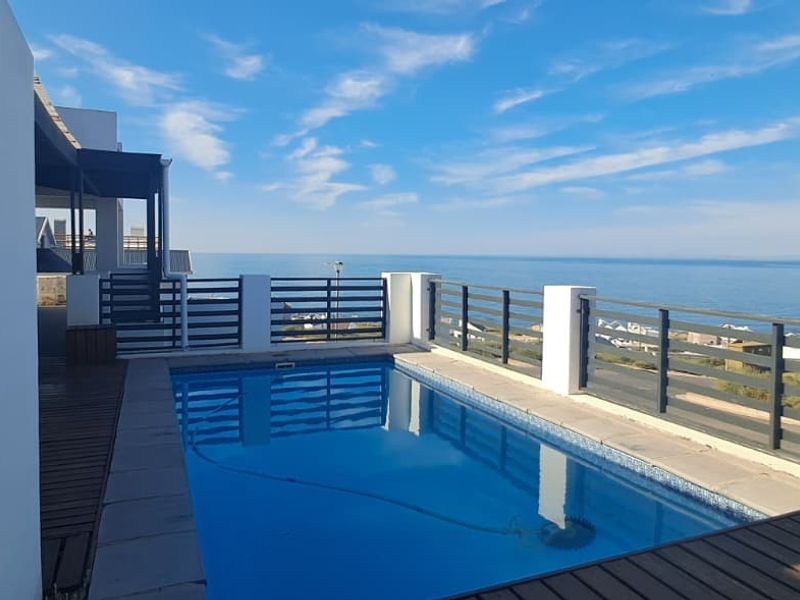 An elevated outdoor pool area featuring timber decking, a modern metal balustrade, and a pergola, offering expansive ocean views.