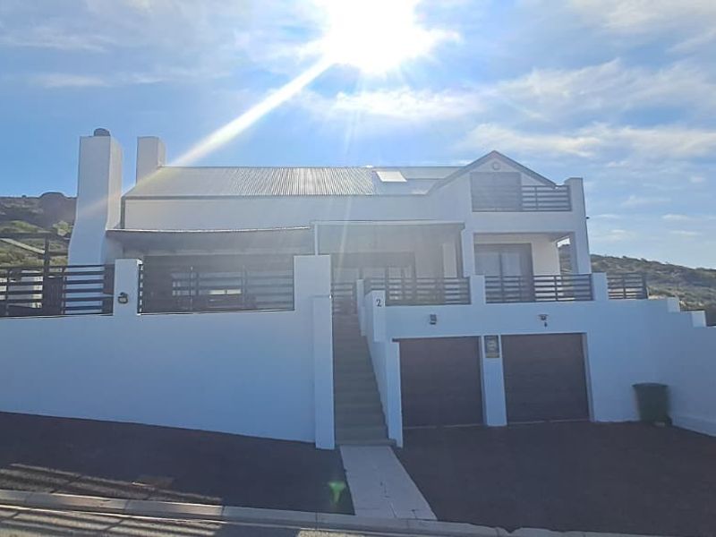 Front elevation of a multi-level house featuring a double garage, balcony, and white exterior finish with a paved driveway.