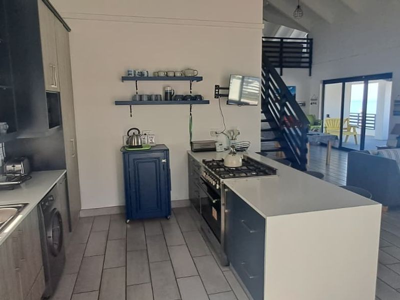 Open-plan kitchen and living area featuring modern cabinetry, gas hob, tiled floors, and direct access to a patio with ocean views.