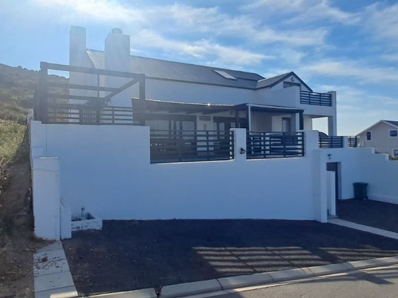 Front elevation of a multi-level house featuring a timber deck, black metal balustrades, and a gravel driveway with a retaining wall.