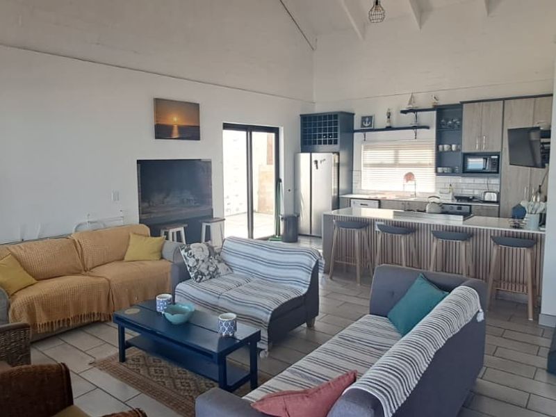 Spacious open-plan living area featuring a modern kitchen with island, vaulted ceilings, tiled floors, and direct access to an outdoor patio.