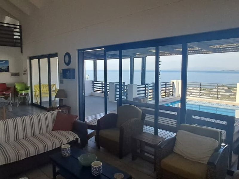 Spacious open-plan living area featuring vaulted ceilings, tiled floors, and large sliding glass doors opening onto a pool deck with expansive ocean views.