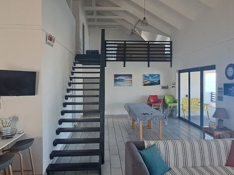 Spacious open-plan living area featuring a vaulted ceiling with exposed rafters, a modern metal staircase leading to a mezzanine, and large sliding doors.